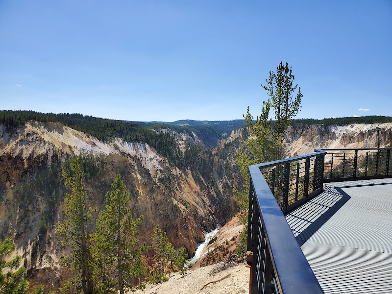 Inspiration Point overlook in Yellowstone National Park with a metal railing, canyon walls, pines, and a river below.