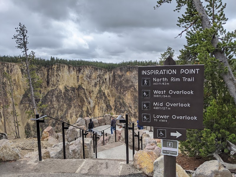 Stone platform overlook with metal railing at Inspiration Point, Yellowstone National Park, offering views of canyon cliffs and pine forests.