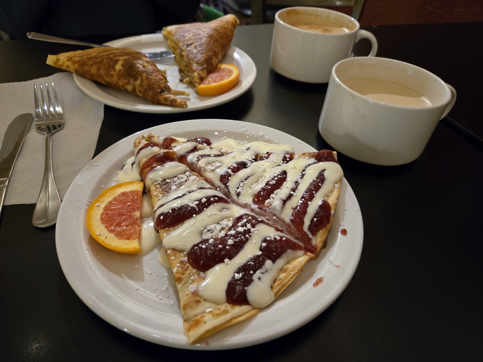 Glacier National Park cafe plate with berry-topped crepes drizzled in white sauce and a orange wedge