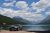 Bowman Lake shoreline with a parked SUV and distant jagged peaks rising above Glacier National Park.