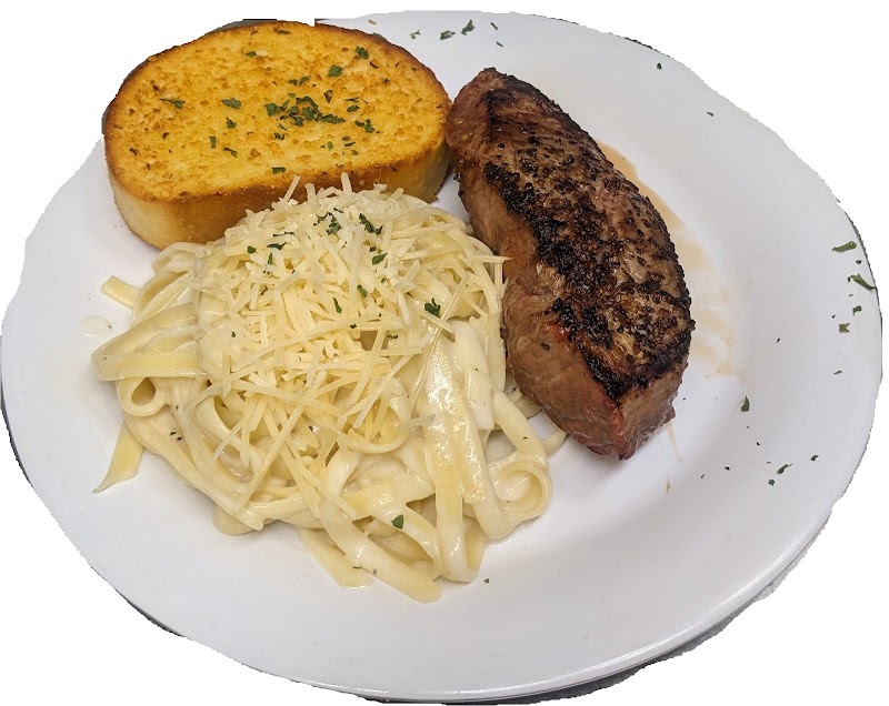 Plate with grilled steak, creamy fettuccine Alfredo topped with grated cheese, and garlic bread in Yellowstone National Park.