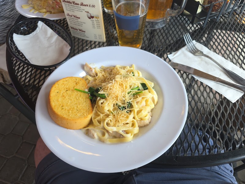 Fettuccine Alfredo with grated cheese and a round garlic bread slice on a metal patio table in Yellowstone National Park.