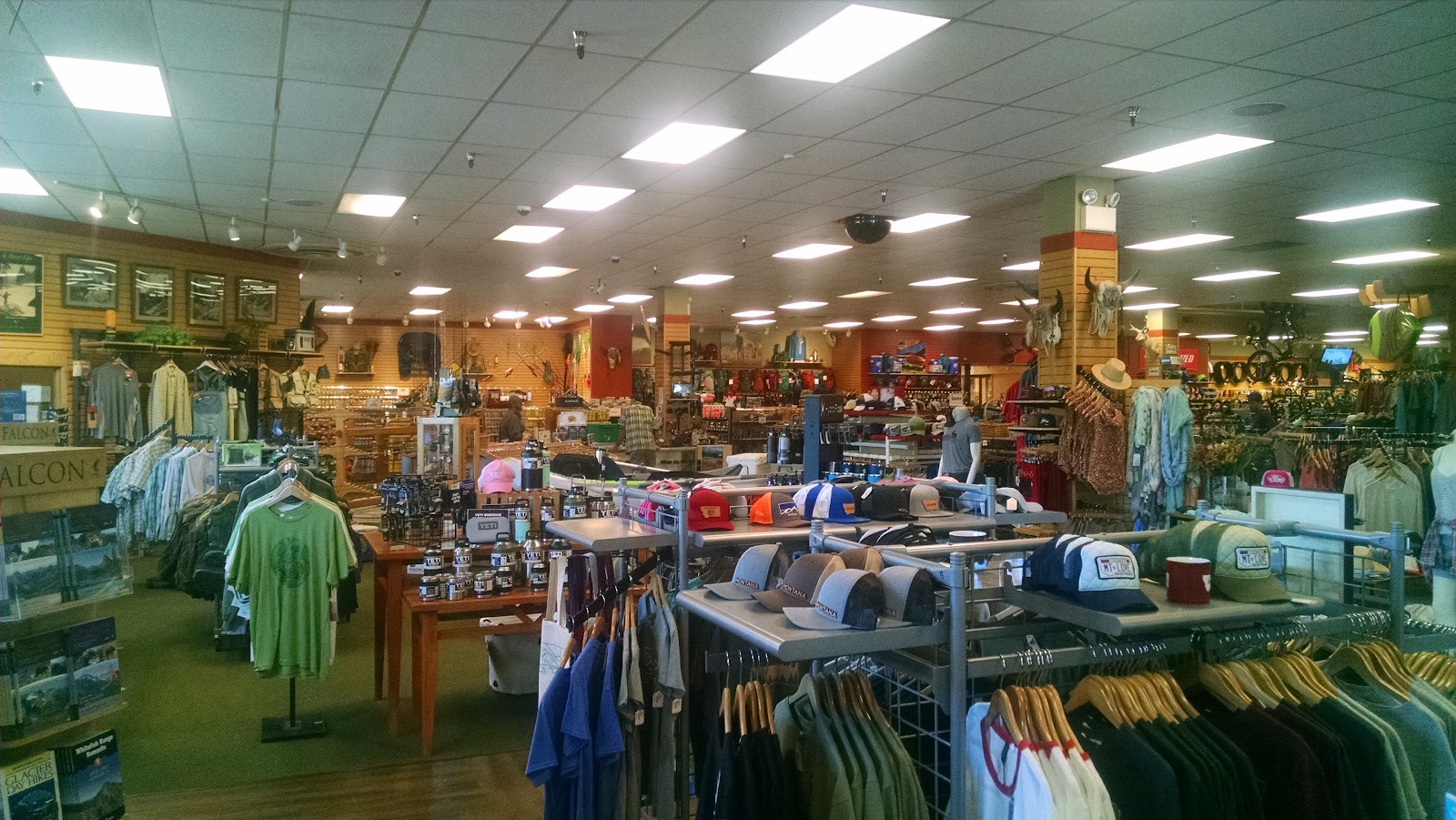 Inside the Glacier National Park gift shop, showcasing clothing racks, hats, and outdoor gear at a busy retail space.