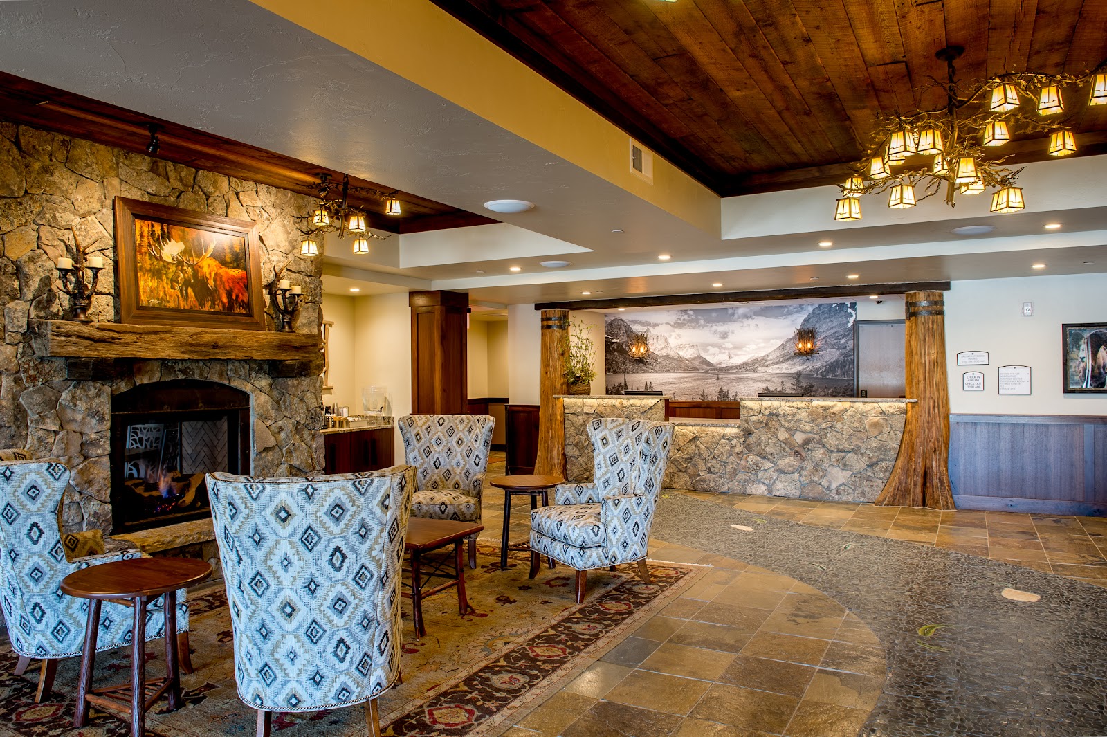 Lodge lobby with a stone fireplace, rustic wood beams, and patterned blue chairs in Glacier National Park.