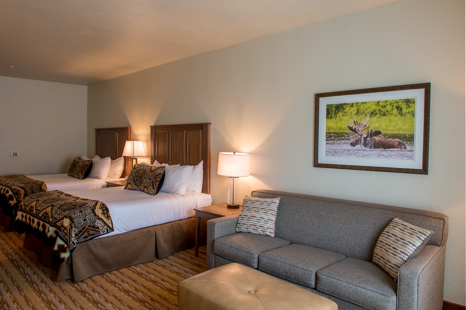 Two-queen bed lodging room in Glacier National Park with a sofa and warm lighting.