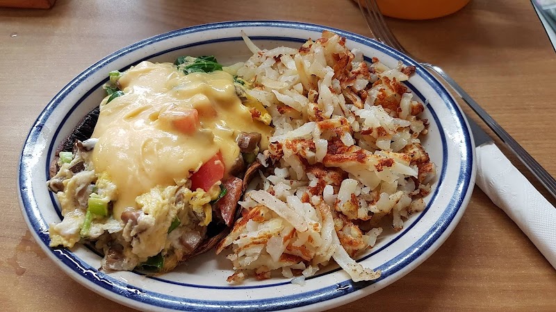 Blue-rimmed plate holds a veggie omelette topped with cheese and a side of browned hash browns, in Yellowstone National Park.