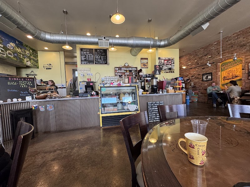 Inside a cozy cafe in Yellowstone National Park: long counter, pastry case, brick walls, exposed ducts, and a round table with a mug.