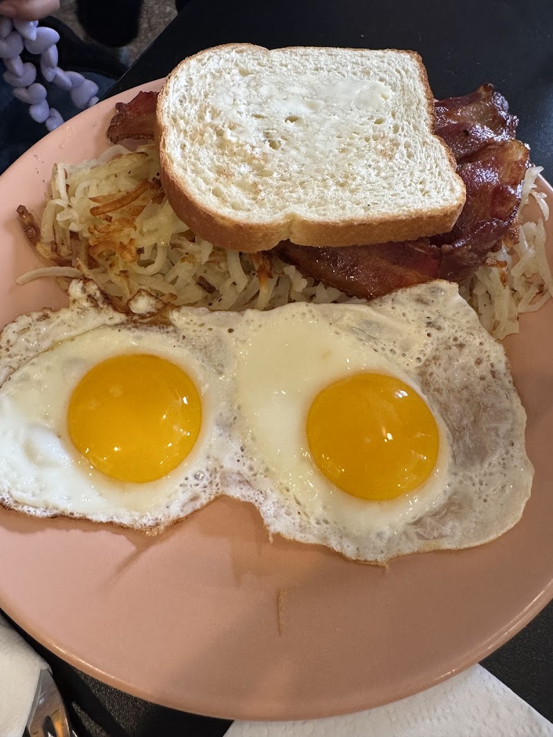 Plate with two sunny-side-up eggs, hash browns, bacon, and toasted bread on a pink plate in Yellowstone National Park.
