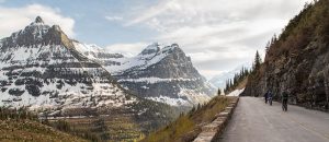 Going-to-the-Sun Road winds along a rock face with snow-capped peaks in Glacier National Park.
