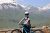 Young rider with helmet on a blue e-bike at a Glacier National Park overlook, snow-capped peaks in the distance.