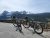 Two e-bikes rest on a paved overlook with snow-capped peaks and dense evergreen forest in Glacier National Park.