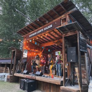 Rustic open-air stage at a wooden saloon in Glacier National Park hosting a live band.
