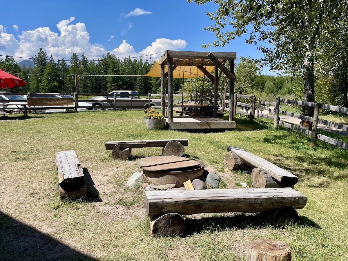 Outdoor seating area at Glacier National Park featuring a wooden gazebo, benches, and a central fire pit.