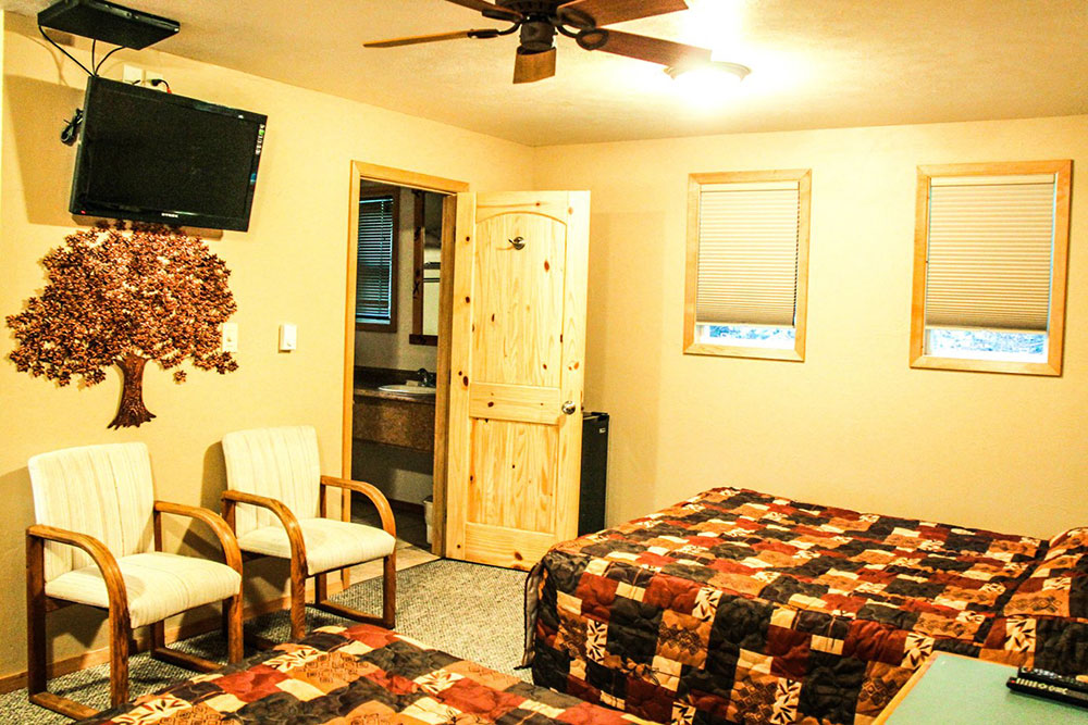 Cozy guest room at Glacier Highland in Glacier National Park with two armchairs, quilted bedspreads, and a ceiling fan.