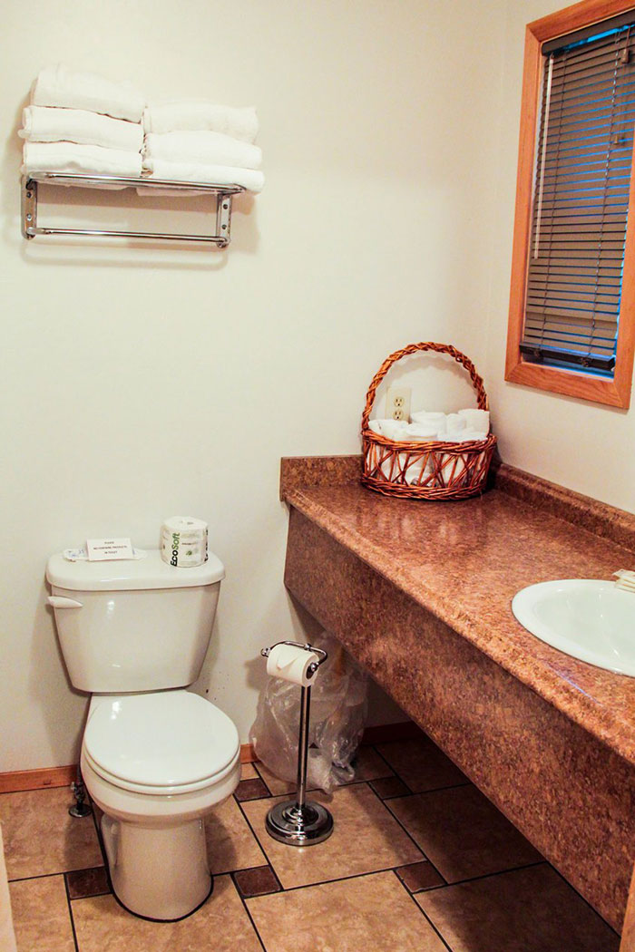 Guest bathroom in Glacier National Park lodging features a toilet, sink, wicker basket, and towel shelves.