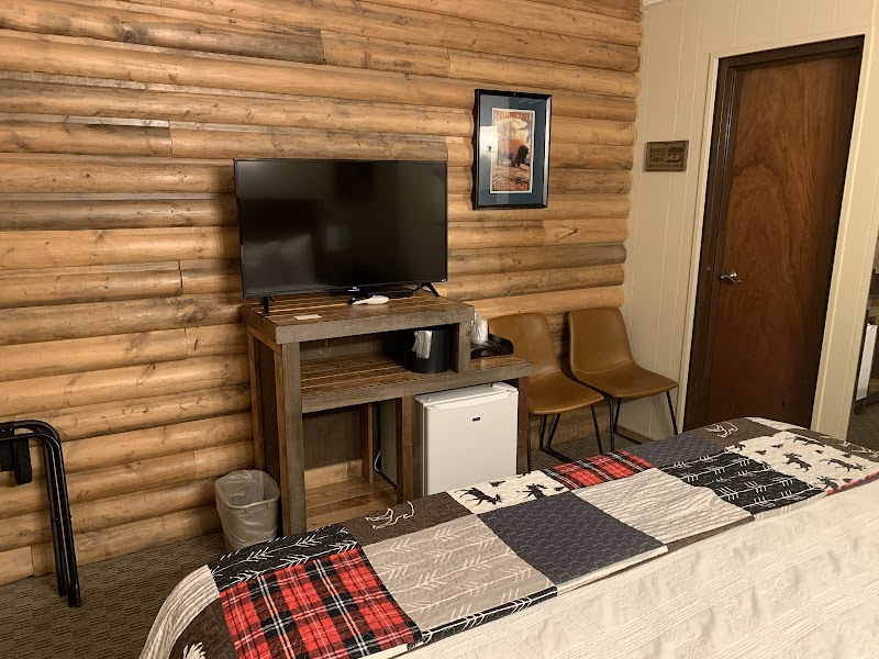 Cozy lodge room with log walls, a flat-screen TV on a wooden stand, and a quilted bed in Yellowstone National Park.