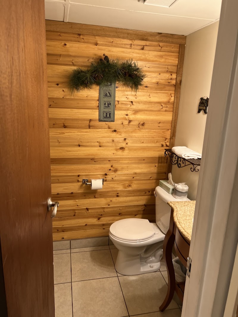 Knotty pine bathroom with a white toilet, tile floor, towel rack, and pine garland above a sign in Yellowstone National Park.