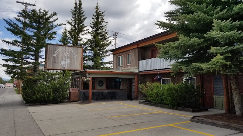 Rustic two-story wood lodge with a covered porch, yellow parking lines, and tall pines in Yellowstone National Park.