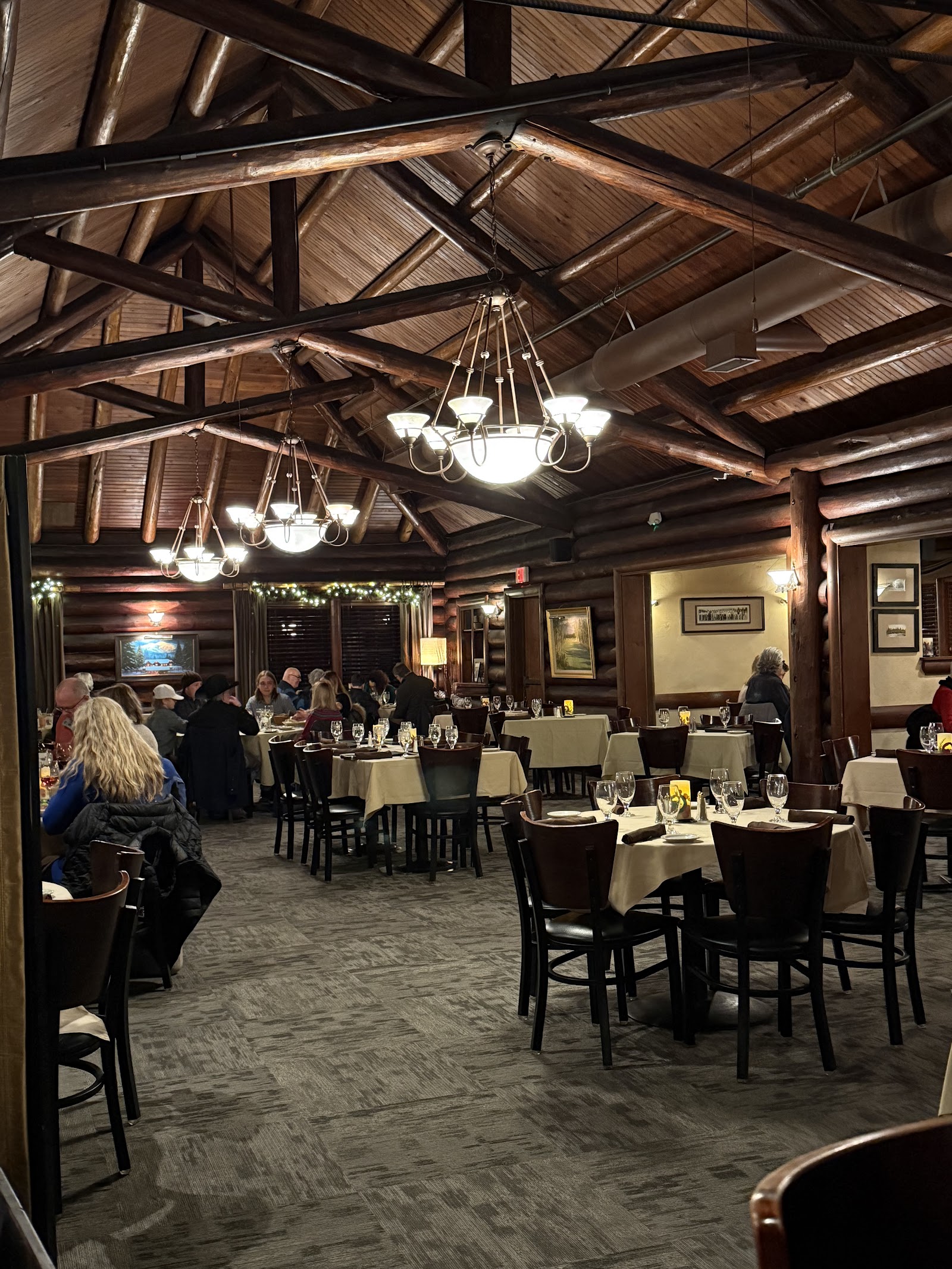 Interior of a rustic lodge-style dining room with heavy log beams and chandeliers in Glacier National Park.