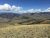 Yellowstone National Park: rolling golden grass hills, distant mountains, blue sky with white clouds, rocky foreground trail.