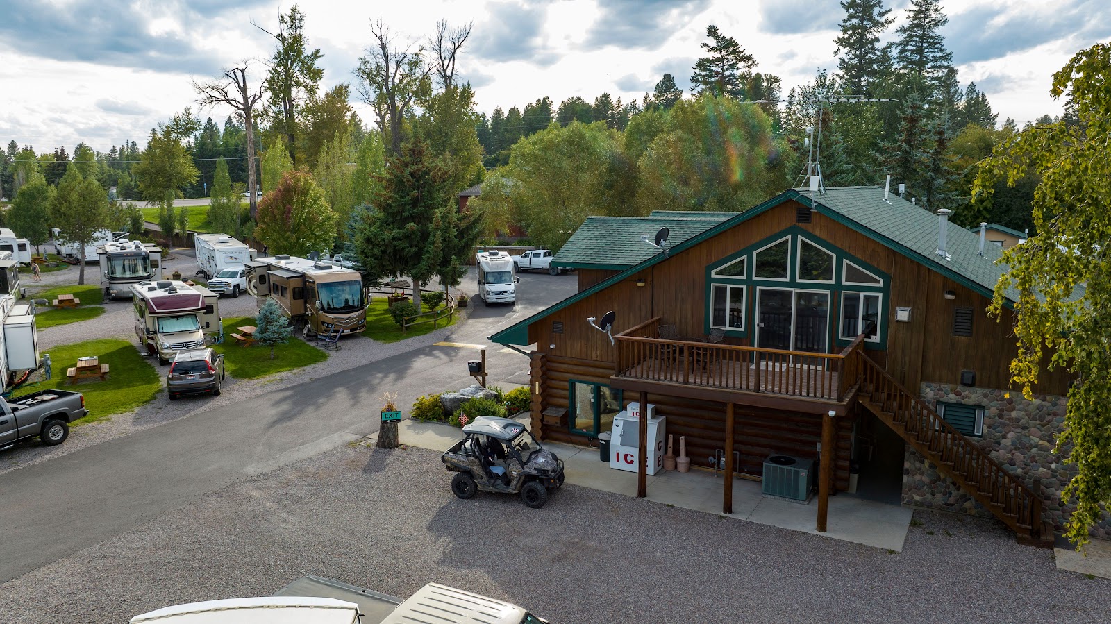 Wooden lodge with green roof and balcony overlooks a campground filled with RVs, cars, and trees in Glacier National Park.