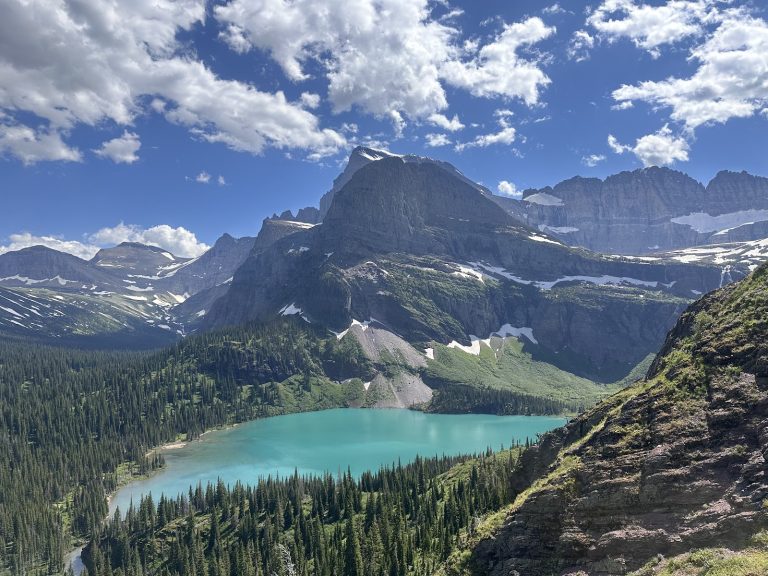 Grinnell Glacier Overlook at Glacier National Park reveals a turquoise lake set against jagged, snow-dusted peaks.