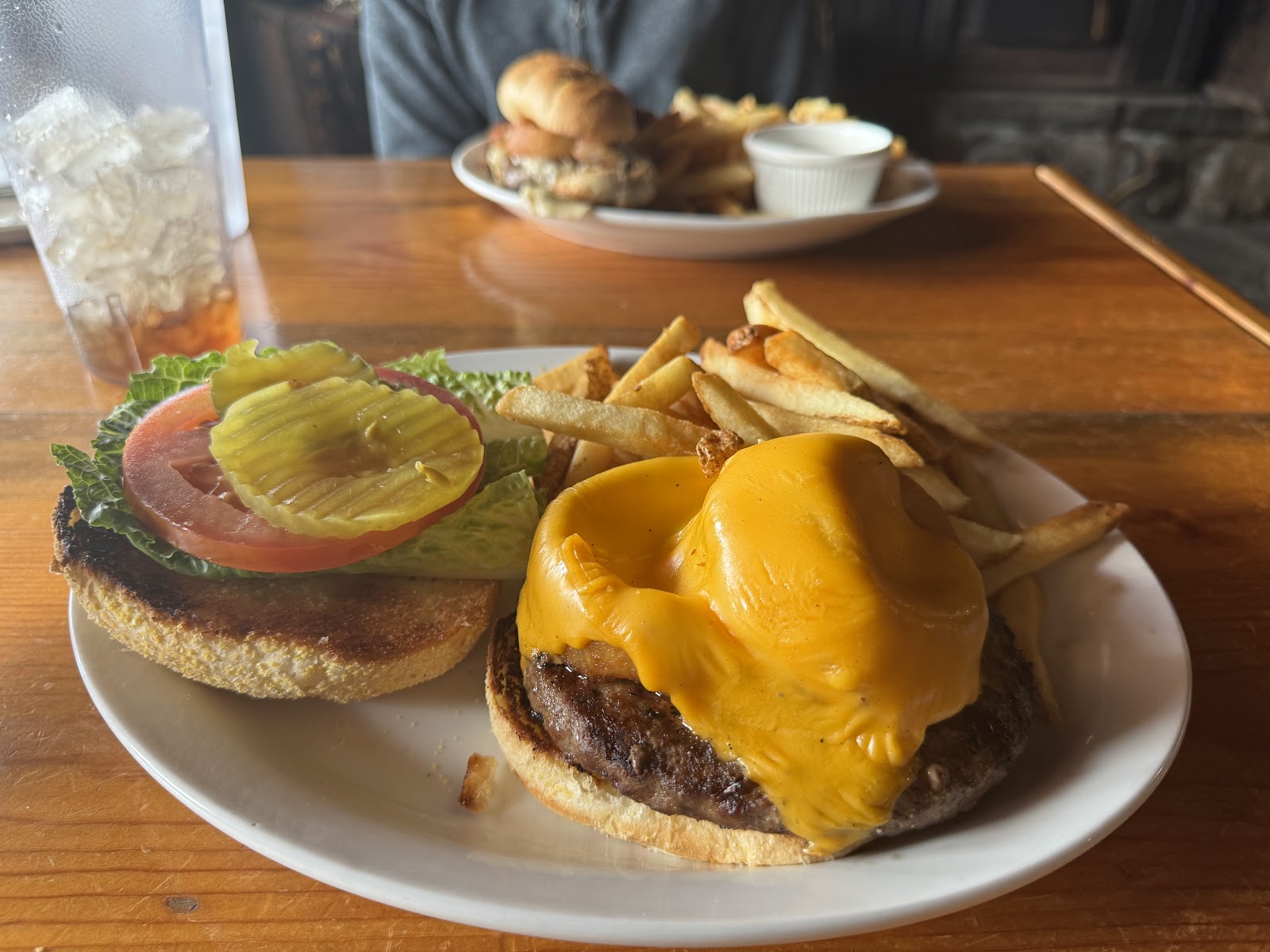 Burger topped with melted cheddar, pickle, tomato, and lettuce with fries on a plate in Glacier National Park.