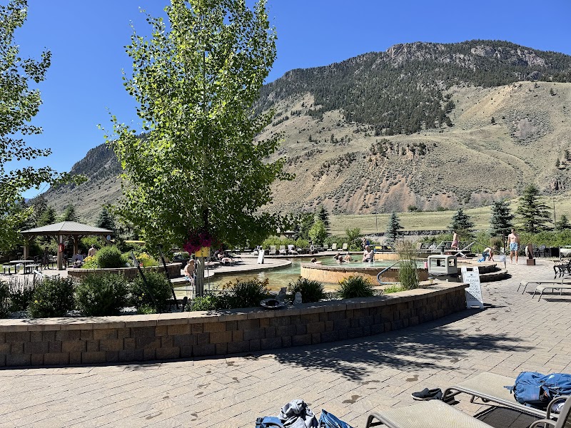 Circular hot springs pools surrounded by stone planters, with visitors and trees against a mountain backdrop in Yellowstone National Park.