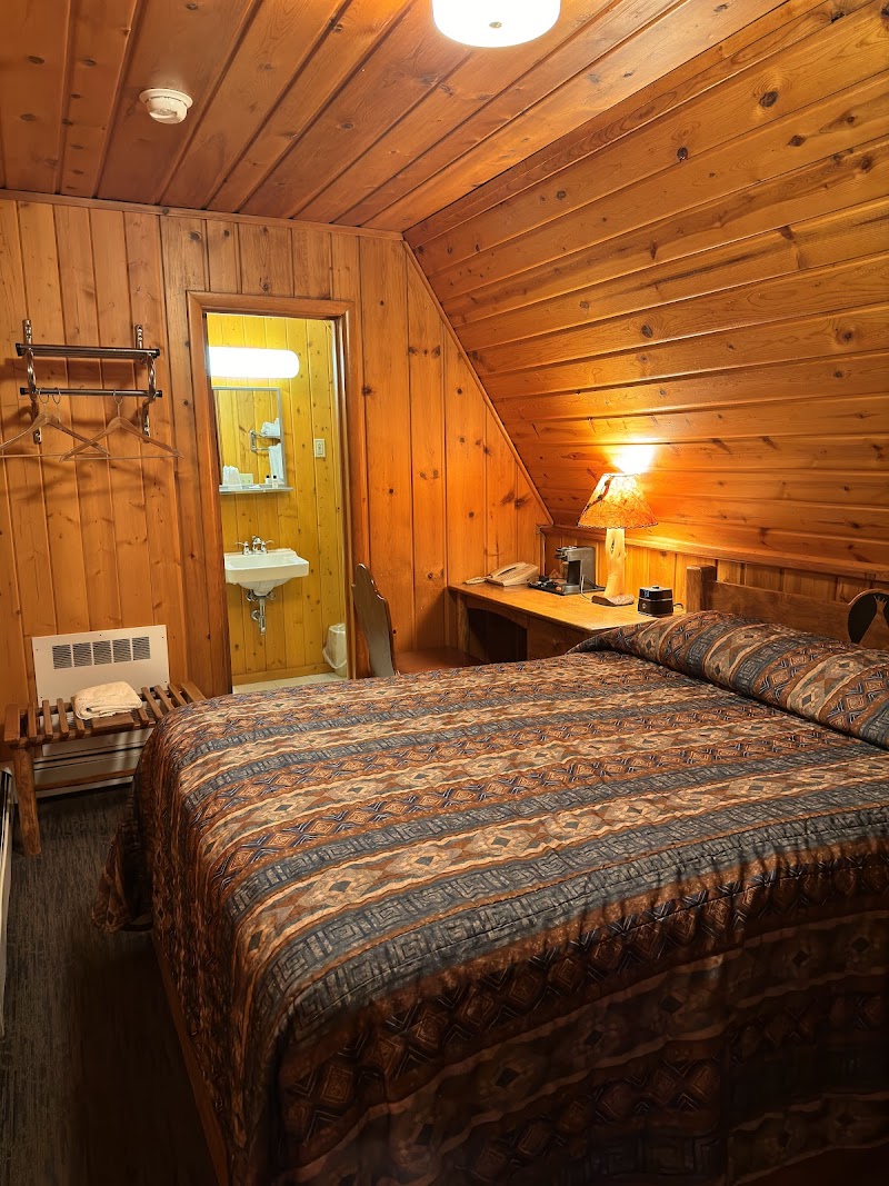 Cozy all-wood lodge room in Yellowstone National Park with two beds, warm patterned quilt, desk, lamp, and an open bathroom doorway.