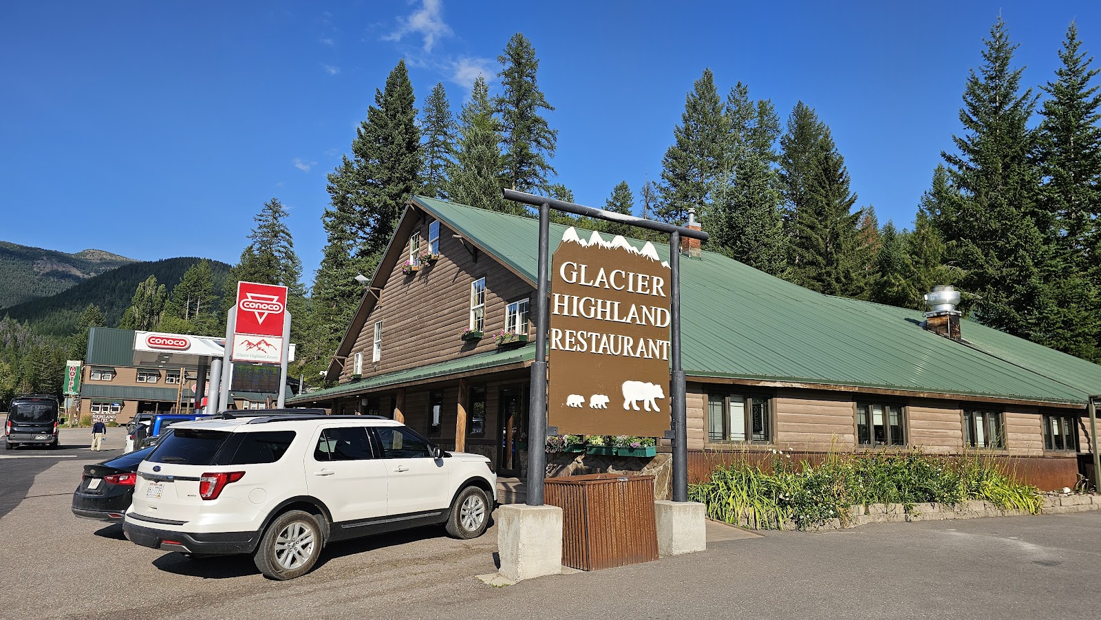 Lodge-style dining lodge at Glacier National Park with a green metal roof, wood siding, and a prominent sign.