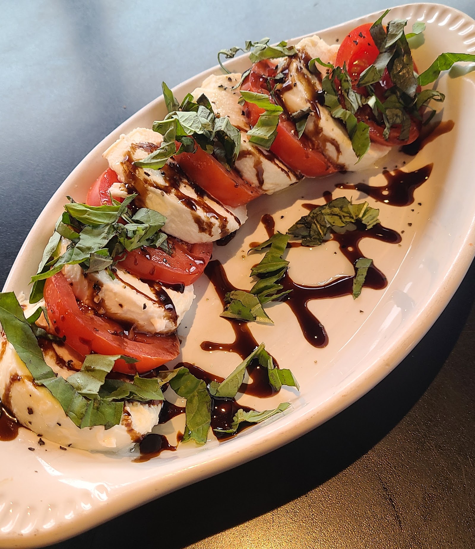 Caprese-style mozzarella and tomato slices with fresh basil on a white oval plate, drizzled with balsamic glaze in Glacier National Park.
