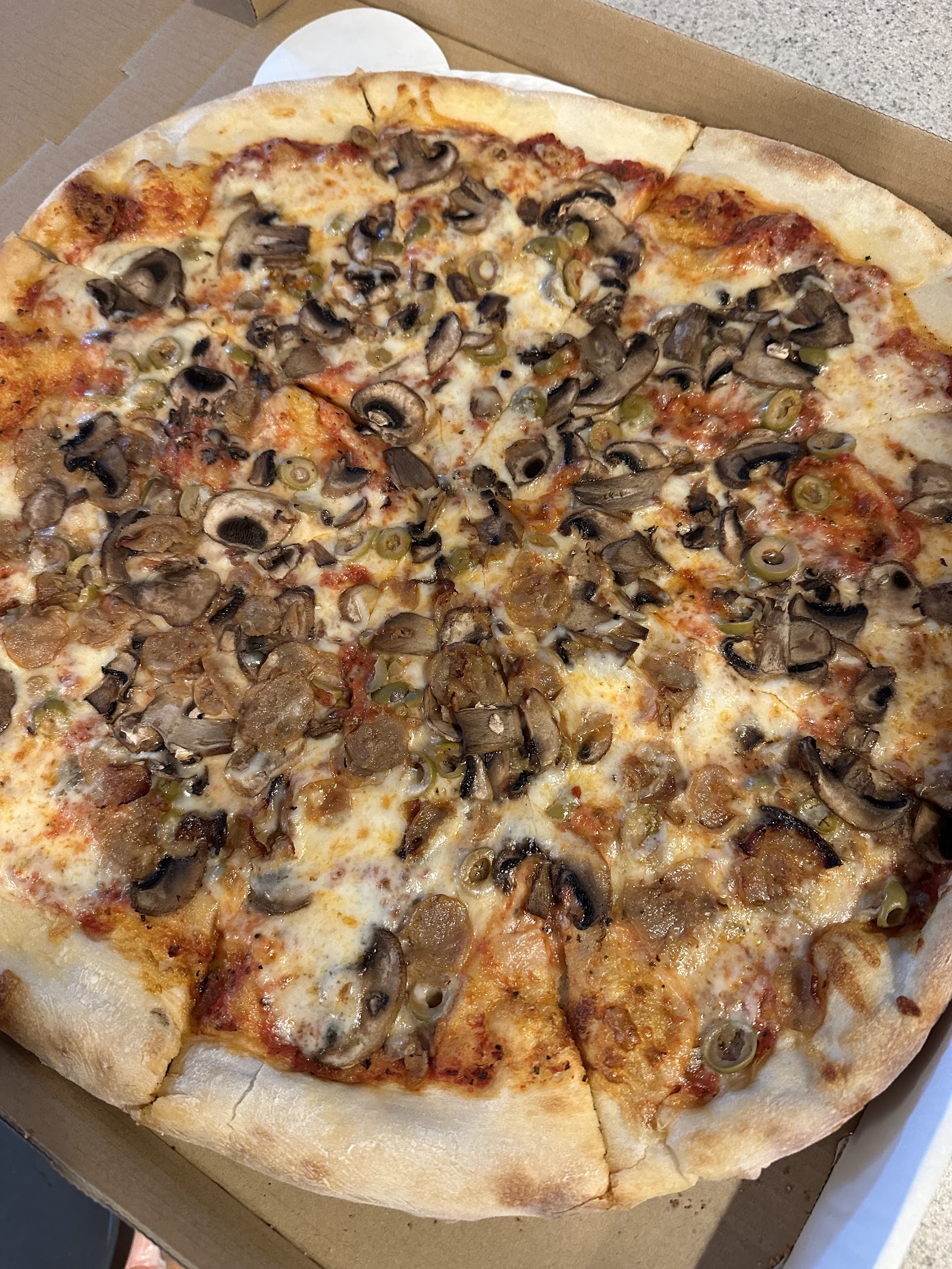 A generously topped mushroom, olive, and pepperoni pizza in a cardboard box, golden crust, Glacier National Park.