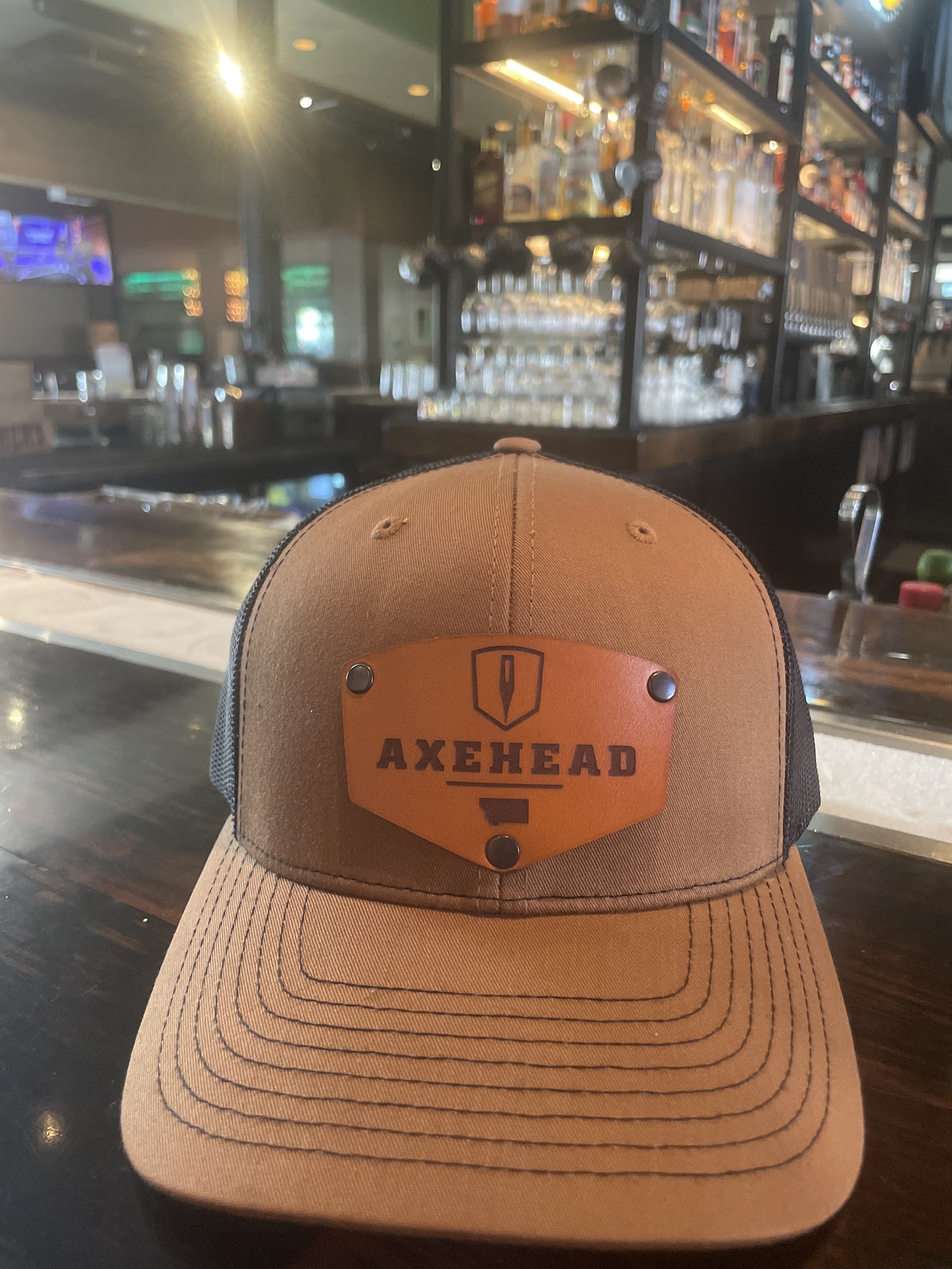 Tan trucker-style cap on a bar counter inside Glacier National Park gift shop, featuring an orange patch on the front.