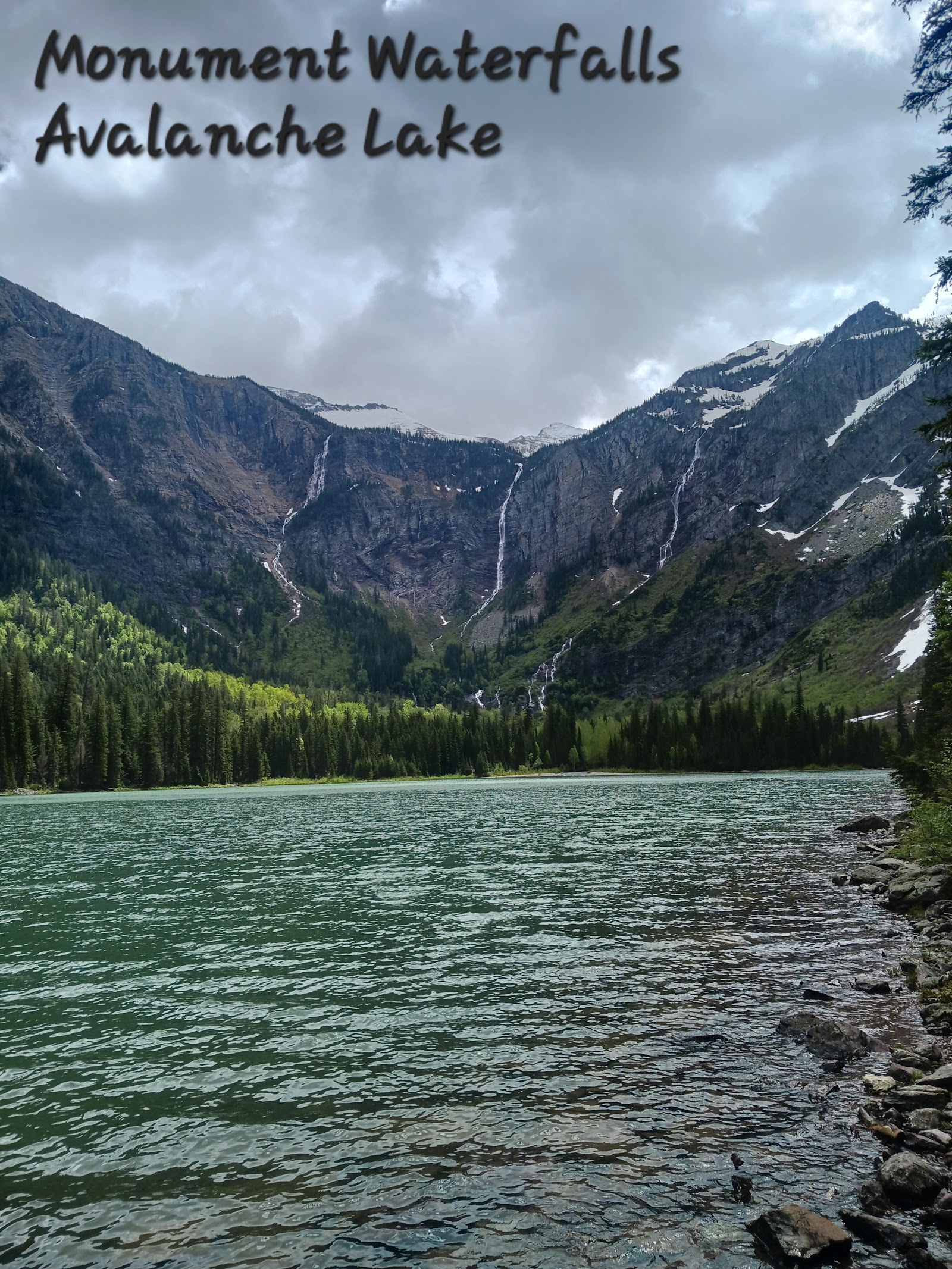Monument Falls cascades beside Avalanche Lake in Glacier National Park, a serene alpine scene.