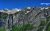Monument Falls drops from rugged granite cliffs in Glacier National Park, with snow patches and a deep blue sky.