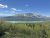 Clear blue sky over snow-capped peaks and a turquoise glacier lake, forested valley from a trail in Glacier National Park.
