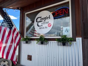 Coffee shop window sign at Glacier National Park with an American flag outside.