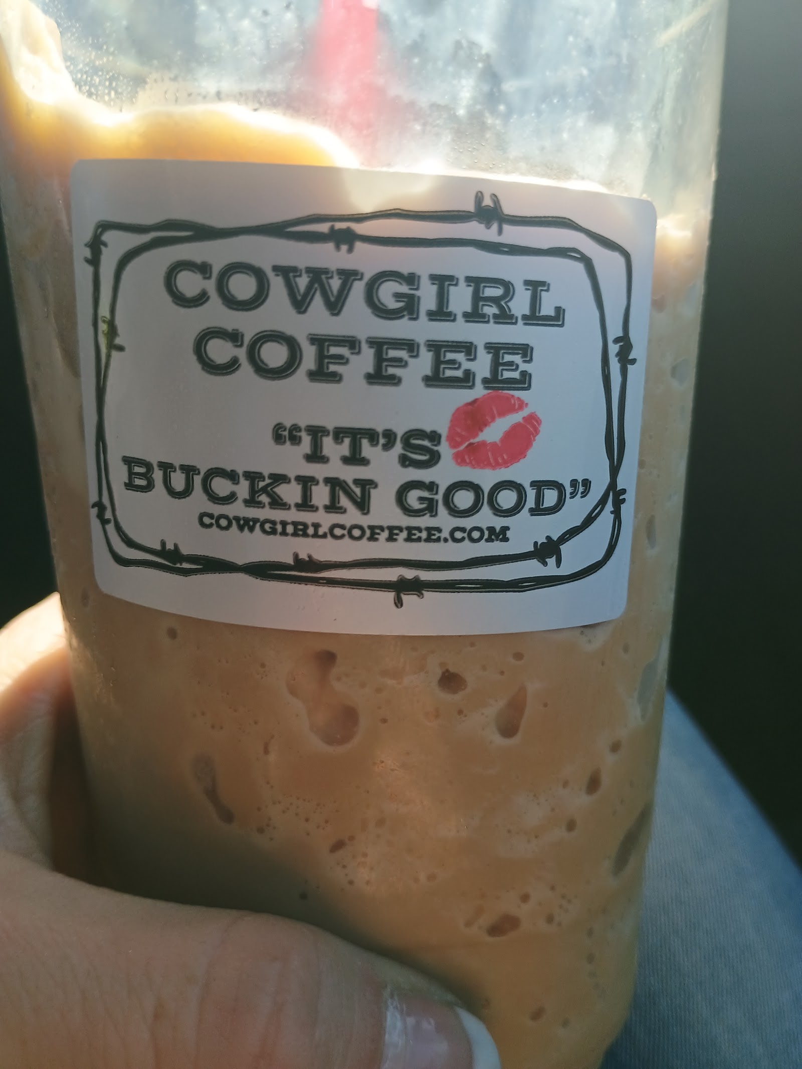Cup with a barbed-wire style label at Glacier National Park, showing a bold sign and frothy coffee behind the glass.
