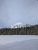 John's Lake with a snow-dusted peak in Glacier National Park, pine forest lining the frozen shoreline.