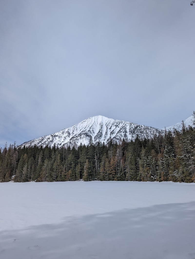John's Lake with a snow-dusted peak in Glacier National Park, pine forest lining the frozen shoreline.