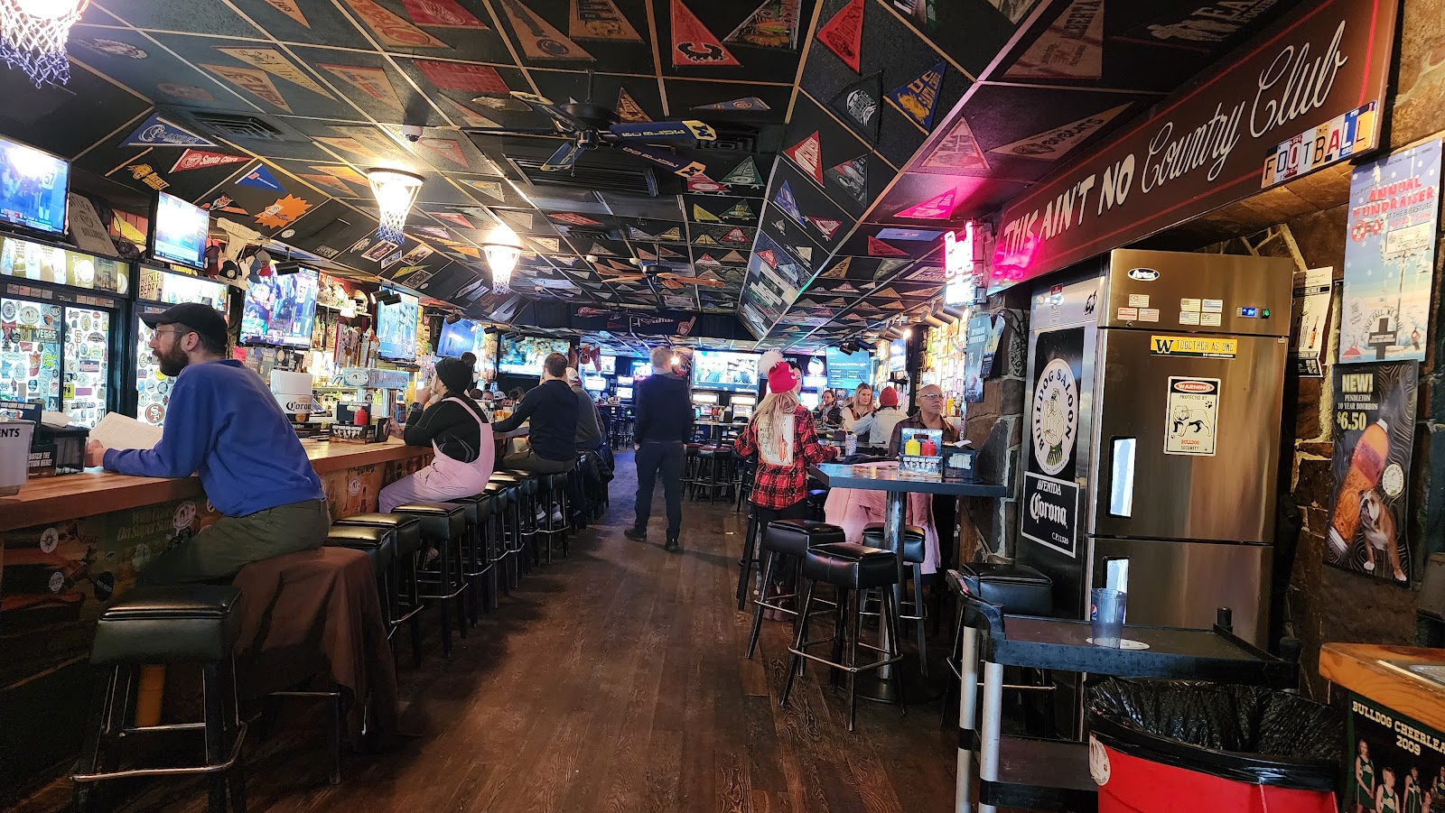 Interior of a rustic bar in Glacier National Park, with sports banners on the ceiling and patrons seated at the counter.