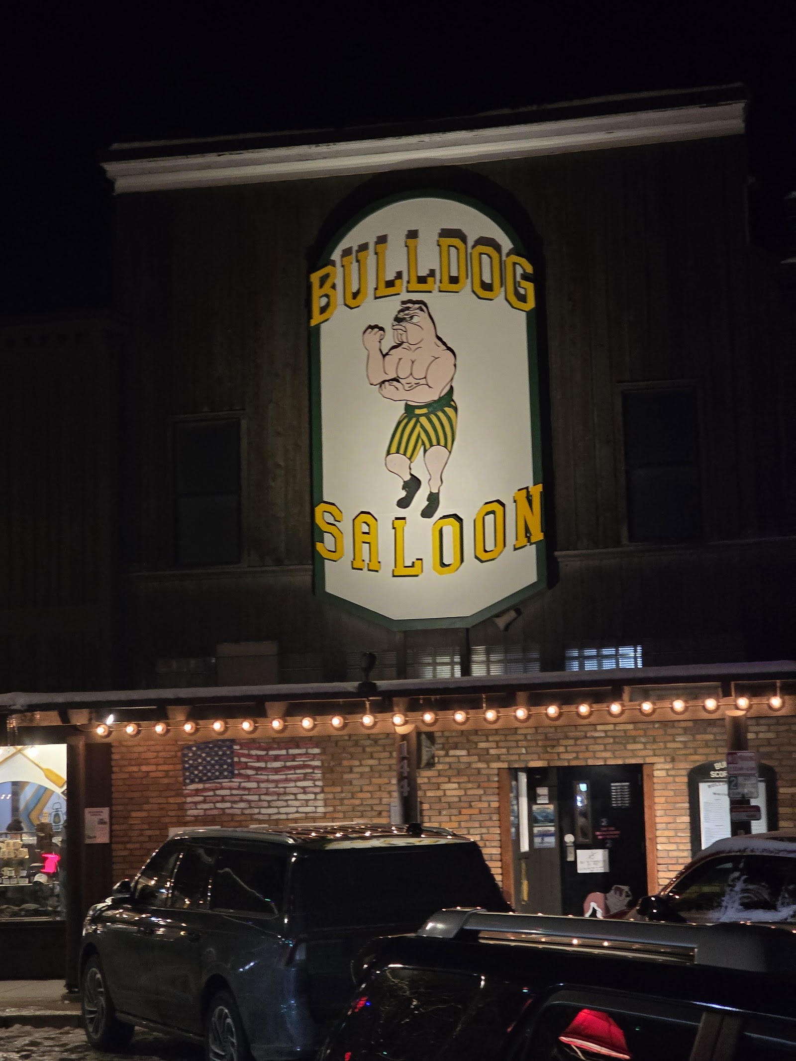 Historic saloon storefront lit at night with a large sign on a wooden facade in Glacier National Park.