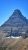 Flinsch Peak towers above rugged Glacier National Park terrain under a bright blue sky.
