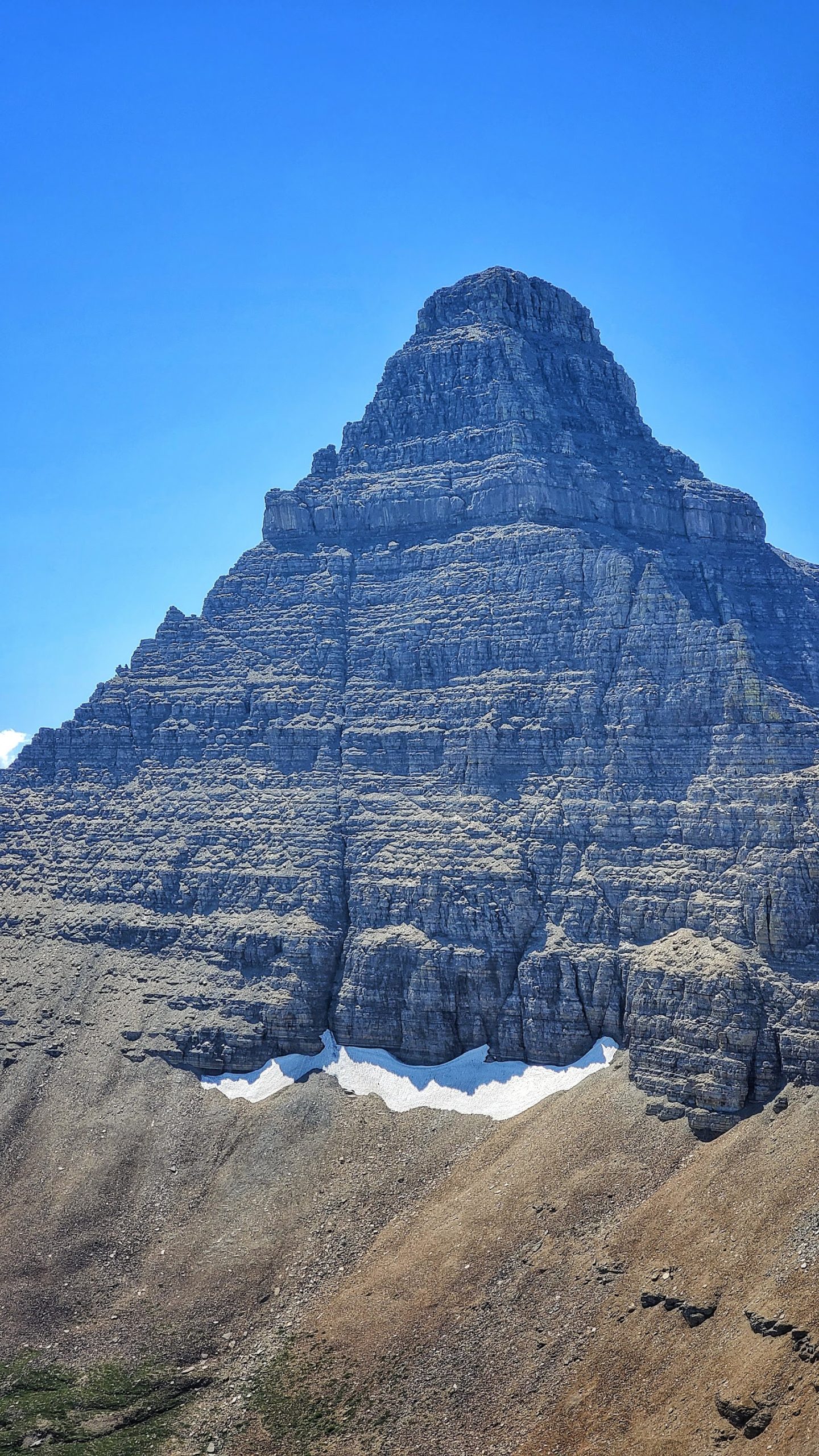 Flinsch Peak towers above rugged Glacier National Park terrain under a bright blue sky.