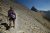 Hiker on a rocky trail near Flinsch Peak in Glacier National Park, with a steep scree slope and rugged basin in the distance.