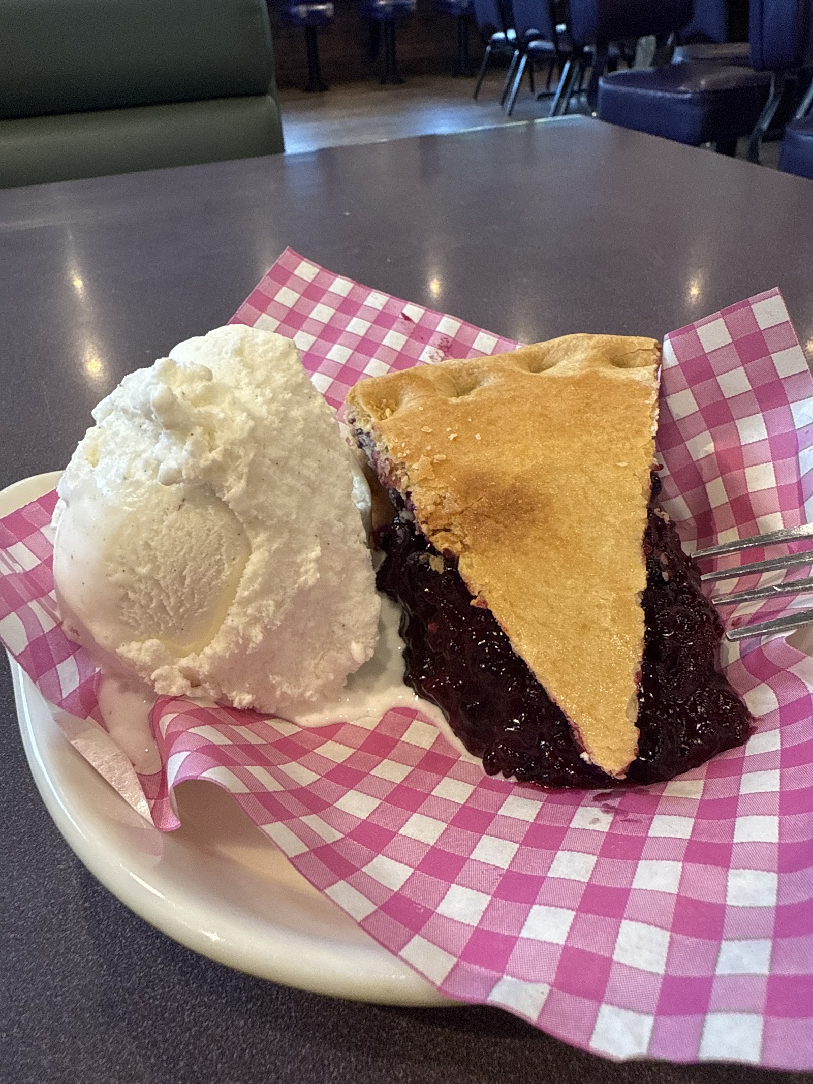 Blueberry pie with vanilla ice cream served on a pink checkered napkin at Glacier National Park restaurant.