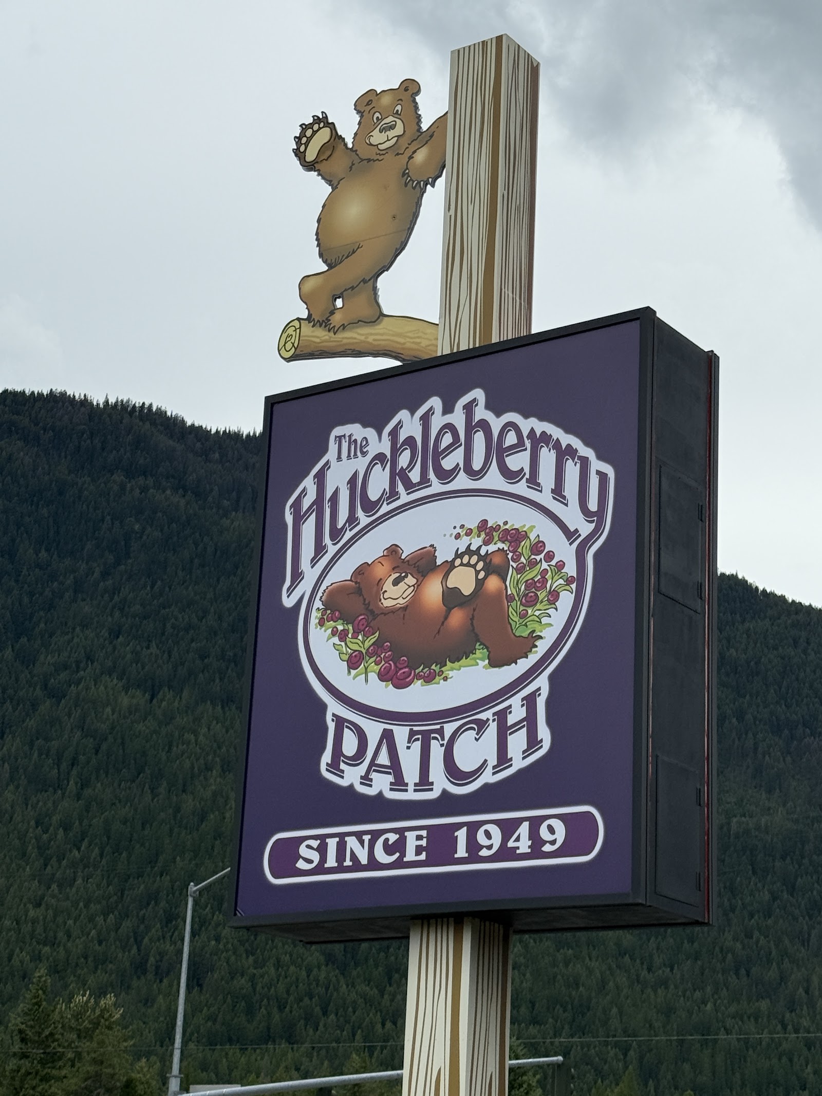 The Huckleberry Patch sign at a Glacier National Park restaurant, featuring a brown bear illustration and a purple panel.