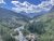 Glacier National Park valley along Siyeh Pass Trail featuring a rocky stream, dense evergreens, and distant rugged peaks under a bright sky.