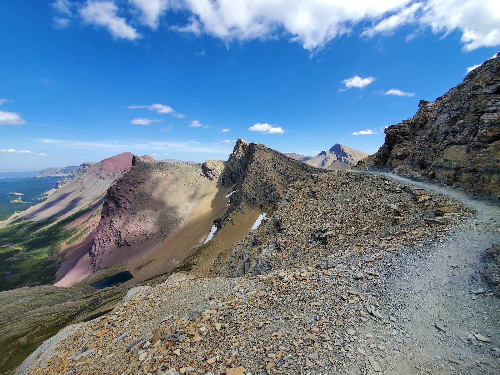 Rugged gravel trail along a ridge on Glacier National Park's Siyeh Pass Trail, with jagged cliffs and distant peaks.