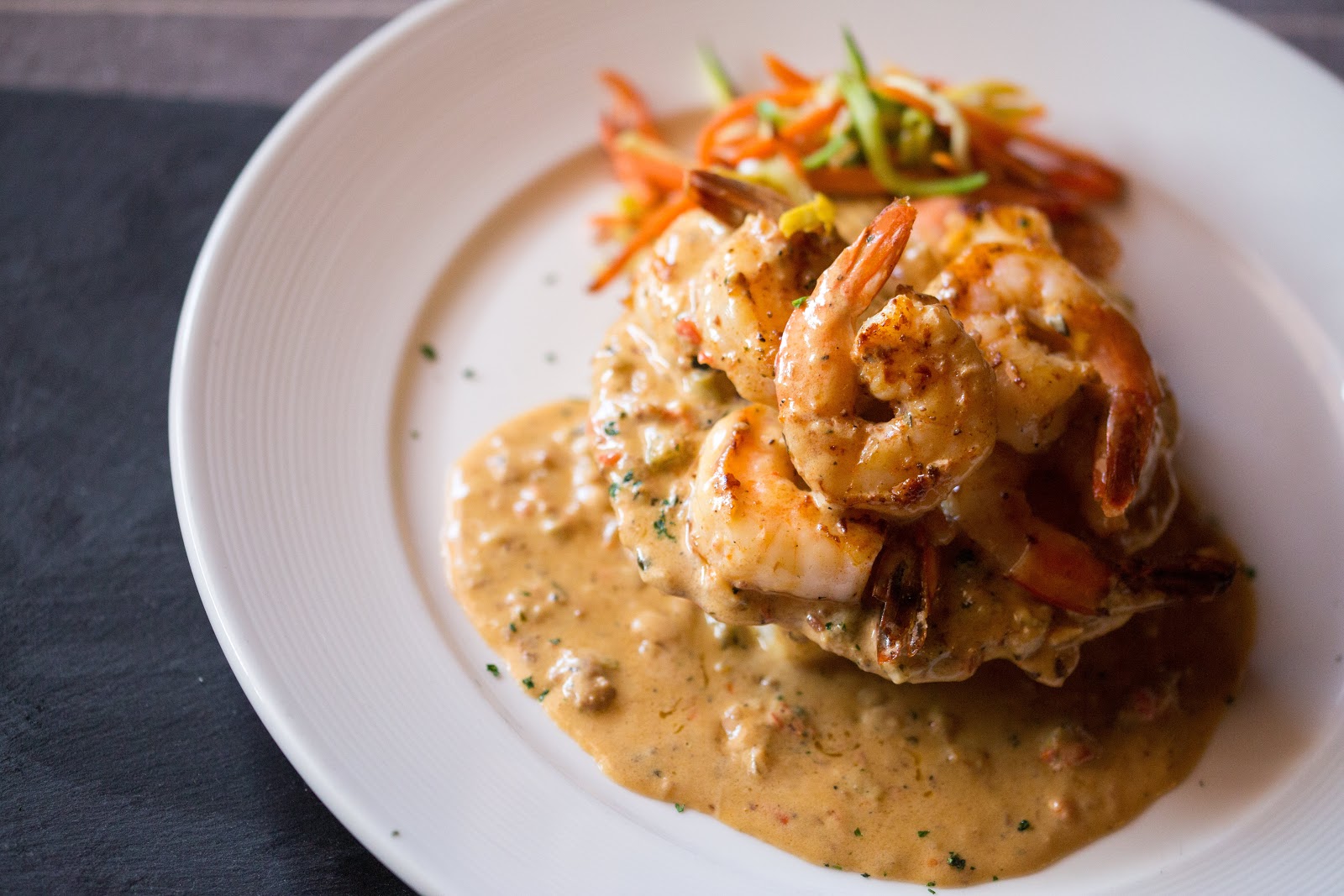 Grilled shrimp in a rich creamy sauce piled on a white plate with carrot slaw garnish in Glacier National Park.